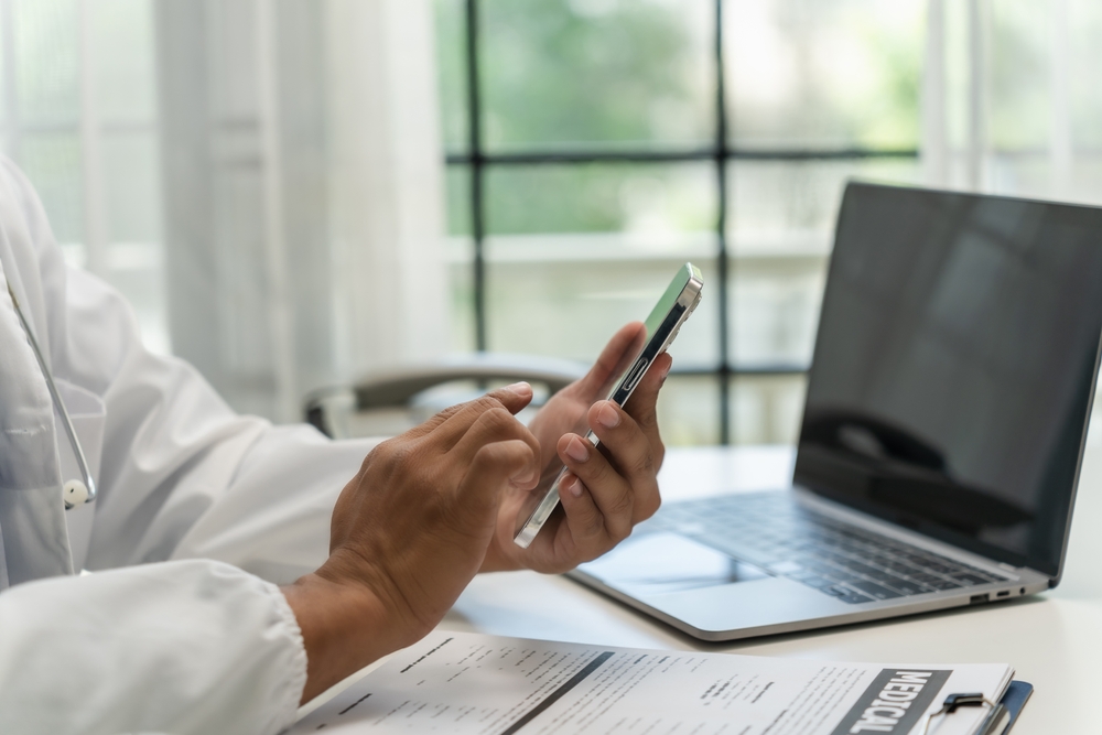 A doctor at a desk is engaged with his phone, possibly checking patient information
