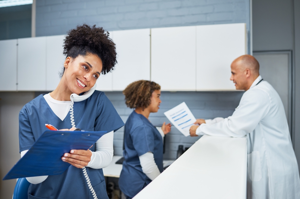 A woman in scrubs is positioned at a counter with two others, participating in a discussion