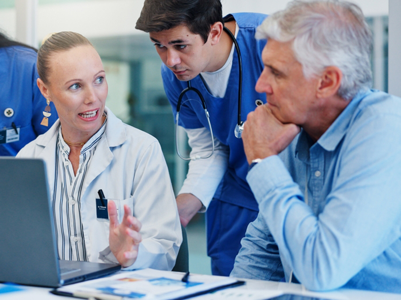 An Asian man in a wheelchair sits beside a nurse, who is engaged in conversation and offering care